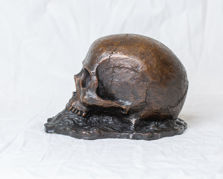 Remember Death bronze skull sculpture by Tom Saxton emerging from textured bronze ground, detailed human skull memento mori sculpture in rich dark bronze, warm copper-brown tones and deep shadowed cavities, contemporary philosophical bronze artwork