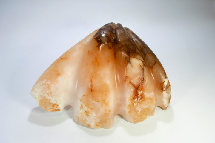 Deborah Harrison sculpture Tear of Joy, a one-off alabaster artwork resembling a shell-like vessel cradling a smooth alabaster sphere. The stone’s warm peach, cream, and brown veining creates a natural marbled effect, suggesting purity, renewal, and the symbolic form of a pearl within a shell.
