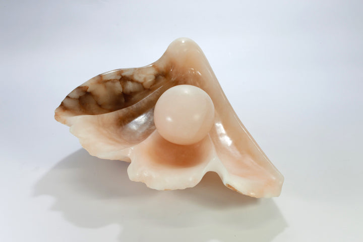 Deborah Harrison sculpture Tear of Joy, a one-off alabaster artwork resembling a shell-like vessel cradling a smooth alabaster sphere. The stone’s warm peach, cream, and brown veining creates a natural marbled effect, suggesting purity, renewal, and the symbolic form of a pearl within a shell.