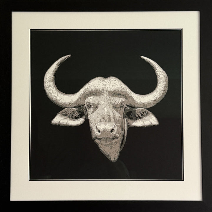 Hand-cut paper artwork of a Cape buffalo head with sweeping horns, crafted from eight layers in tones of ivory, stone grey, and warm taupe. The calm, commanding gaze captures strength and resilience, framed in black wood with UV-protective art glass.