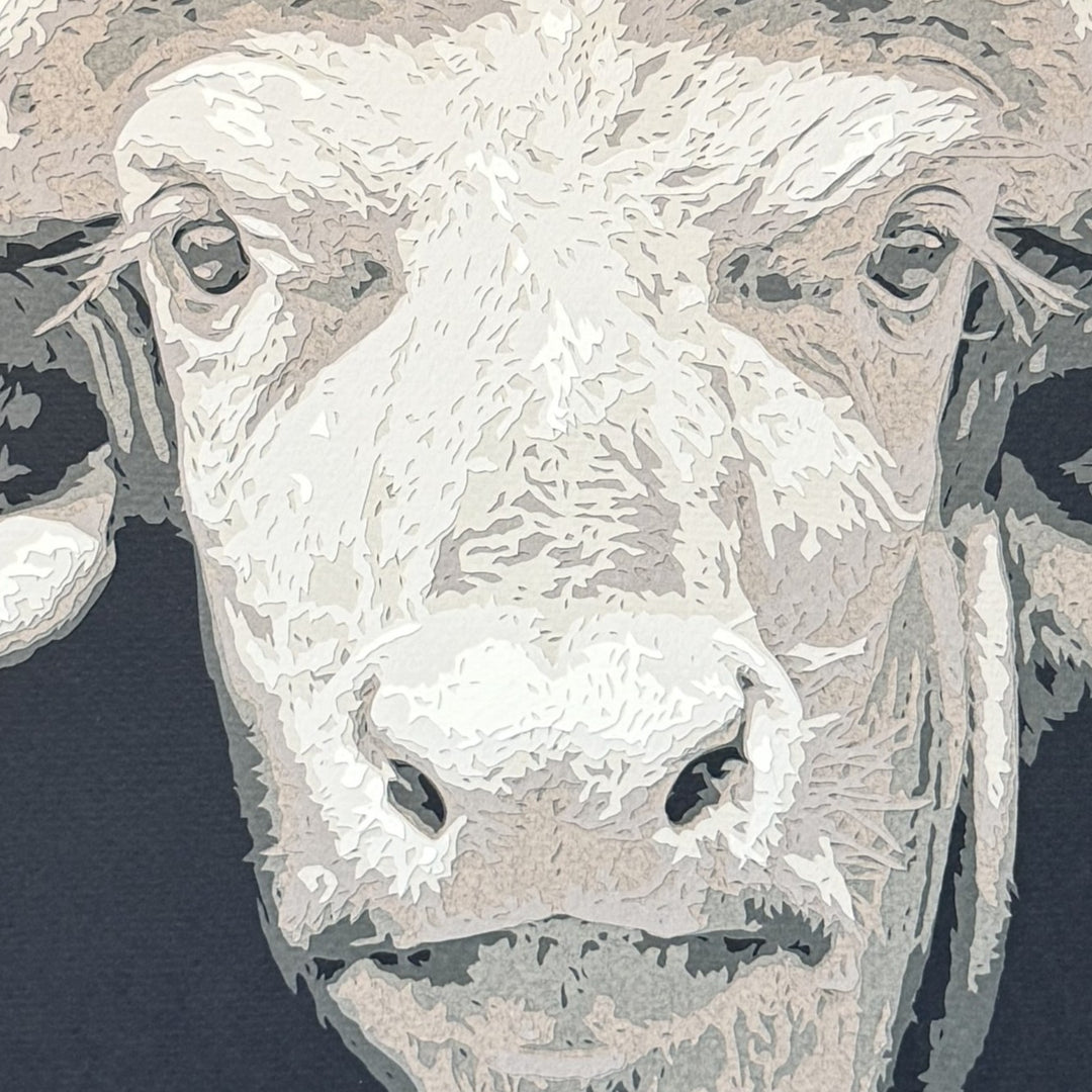 Hand-cut paper artwork of a Cape buffalo head with sweeping horns, crafted from eight layers in tones of ivory, stone grey, and warm taupe. The calm, commanding gaze captures strength and resilience, framed in black wood with UV-protective art glass.