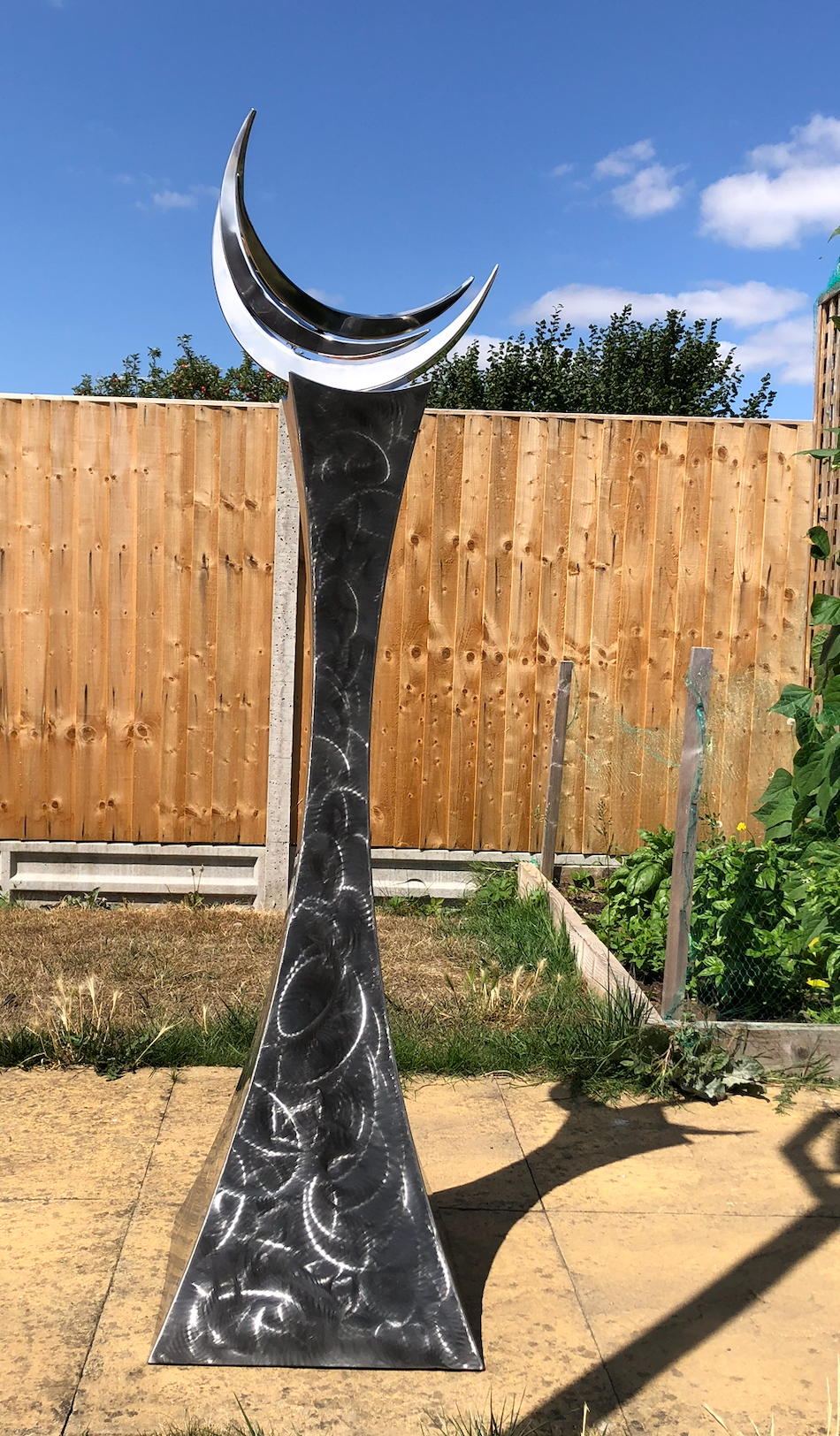 Martin Jarvis’ The Crescent Trinity (Edition 1 of 10), kinetic sculpture in 316 stainless steel with sealed ball race bearings. Standing 1.5m tall, the polished triple crescent form rises from a textured, flared base, rotating gracefully when touched or moved by wind.