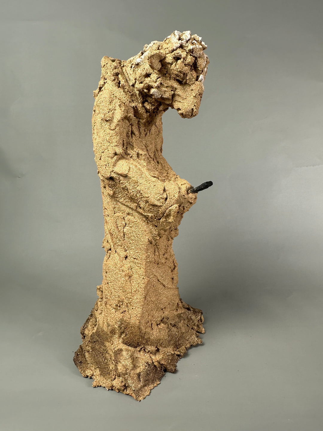 Ceramic figurative sculpture by Eve Shepherd depicting a solitary seated, animal-like figure hunched forward and absorbed in a mobile phone, rendered in rough-textured fired clay with an earthy, sand-coloured surface, capturing contemporary isolation, digital distraction, and quiet introspection through raw, observational form.