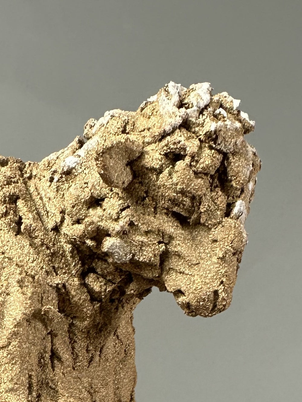 Ceramic figurative sculpture by Eve Shepherd depicting a solitary seated, animal-like figure hunched forward and absorbed in a mobile phone, rendered in rough-textured fired clay with an earthy, sand-coloured surface, capturing contemporary isolation, digital distraction, and quiet introspection through raw, observational form.