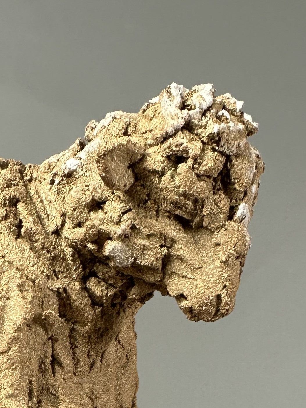 Ceramic figurative sculpture by Eve Shepherd depicting a solitary seated, animal-like figure hunched forward and absorbed in a mobile phone, rendered in rough-textured fired clay with an earthy, sand-coloured surface, capturing contemporary isolation, digital distraction, and quiet introspection through raw, observational form.