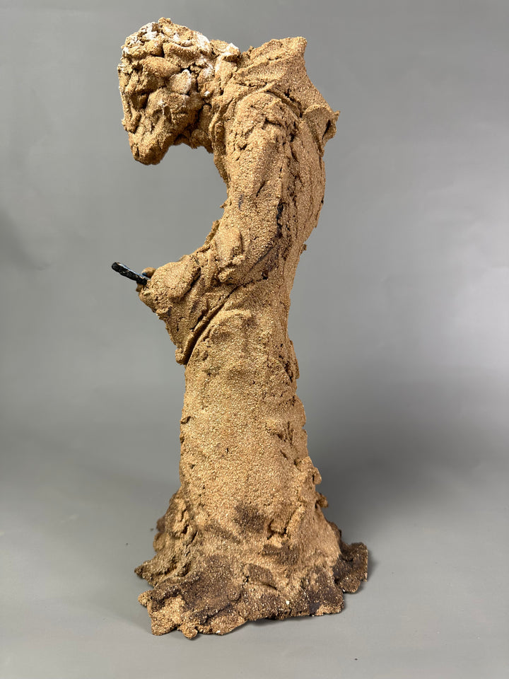 Ceramic figurative sculpture by Eve Shepherd depicting a solitary seated, animal-like figure hunched forward and absorbed in a mobile phone, rendered in rough-textured fired clay with an earthy, sand-coloured surface, capturing contemporary isolation, digital distraction, and quiet introspection through raw, observational form.