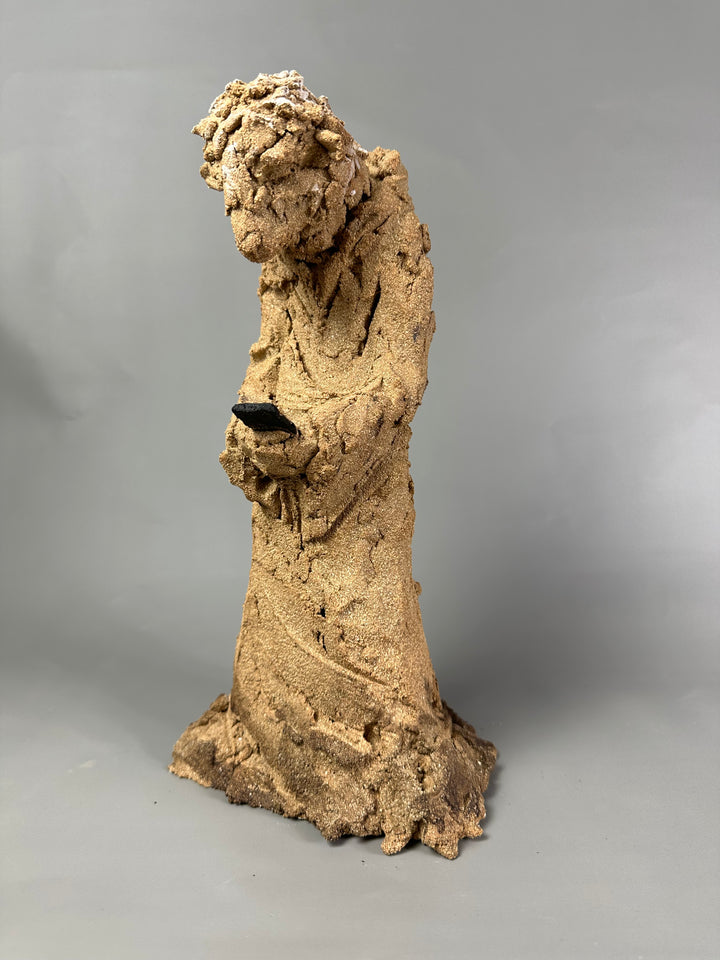 Ceramic figurative sculpture by Eve Shepherd depicting a solitary seated, animal-like figure hunched forward and absorbed in a mobile phone, rendered in rough-textured fired clay with an earthy, sand-coloured surface, capturing contemporary isolation, digital distraction, and quiet introspection through raw, observational form.