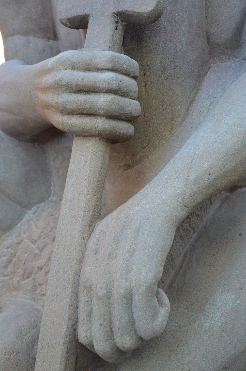 Deborah Harrison sculpture The Guardian, a monumental one-off sandstone figure kneeling with bowed head, gripping a sword planted into the ground. Carved from warm Forest of Dean sandstone, the faceless guardian form conveys strength, sacrifice, and timeless watchfulness, with a skull motif at its base adding symbolism of mortality and protection.