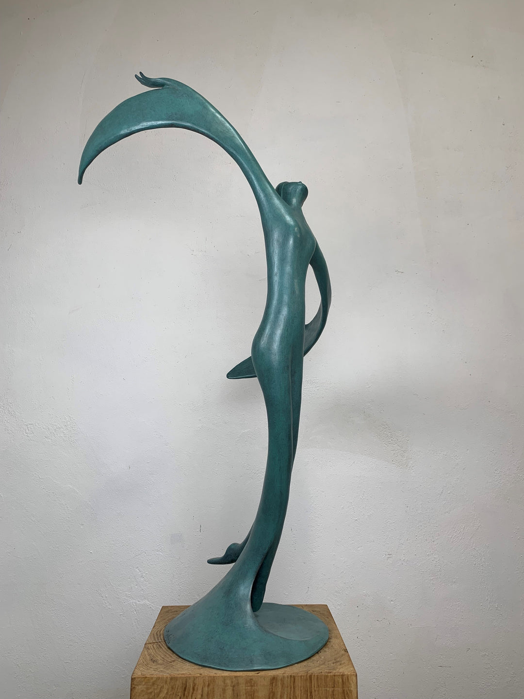 Abstract teal bronze sculpture of a flowing female figure with elongated arms and sweeping wing-like forms, suggesting flight or dance.