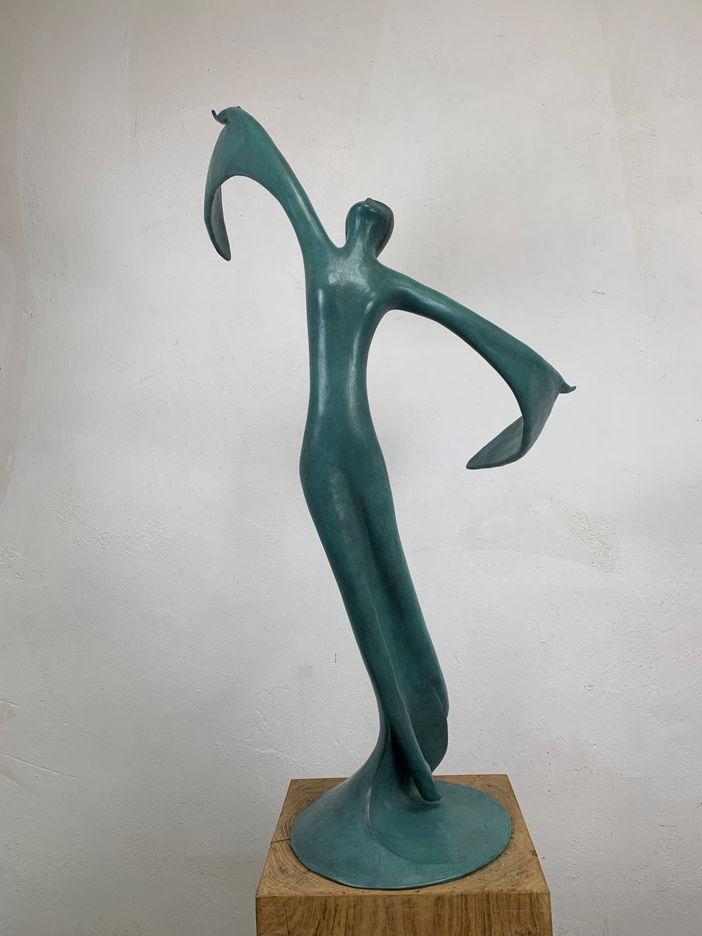 Abstract teal bronze sculpture of a flowing female figure with elongated arms and sweeping wing-like forms, suggesting flight or dance.