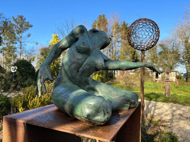 Teresa Wells’ The Wish (2021), limited edition bronze sculpture depicting a seated female figure with one leg folded beneath her and the other extended, torso twisting as she reaches outward with an expressive, outstretched hand. Finished in a mottled green patina with bronze undertones, the piece captures a moment of yearning and emotional intensity, with finely rendered musculature, detailed facial features, and dynamic posture. Measuring 60cm × 37cm × 44cm and weighing 37.3kg.