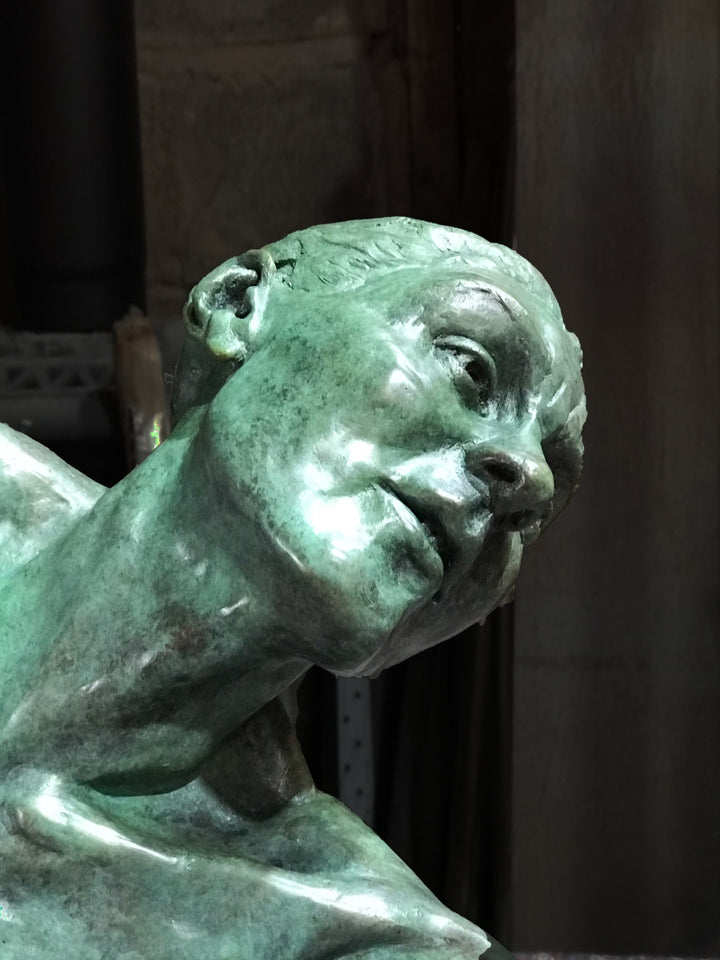 Teresa Wells’ The Wish (2021), limited edition bronze sculpture depicting a seated female figure with one leg folded beneath her and the other extended, torso twisting as she reaches outward with an expressive, outstretched hand. Finished in a mottled green patina with bronze undertones, the piece captures a moment of yearning and emotional intensity, with finely rendered musculature, detailed facial features, and dynamic posture. Measuring 60cm × 37cm × 44cm and weighing 37.3kg.