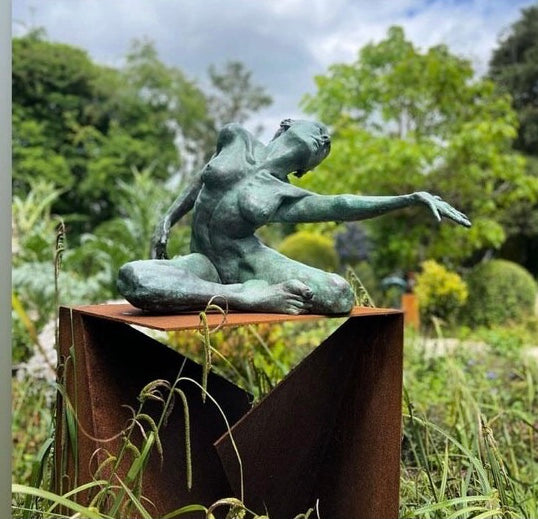 Teresa Wells’ The Wish (2021), limited edition bronze sculpture depicting a seated female figure with one leg folded beneath her and the other extended, torso twisting as she reaches outward with an expressive, outstretched hand. Finished in a mottled green patina with bronze undertones, the piece captures a moment of yearning and emotional intensity, with finely rendered musculature, detailed facial features, and dynamic posture. Measuring 60cm × 37cm × 44cm and weighing 37.3kg.