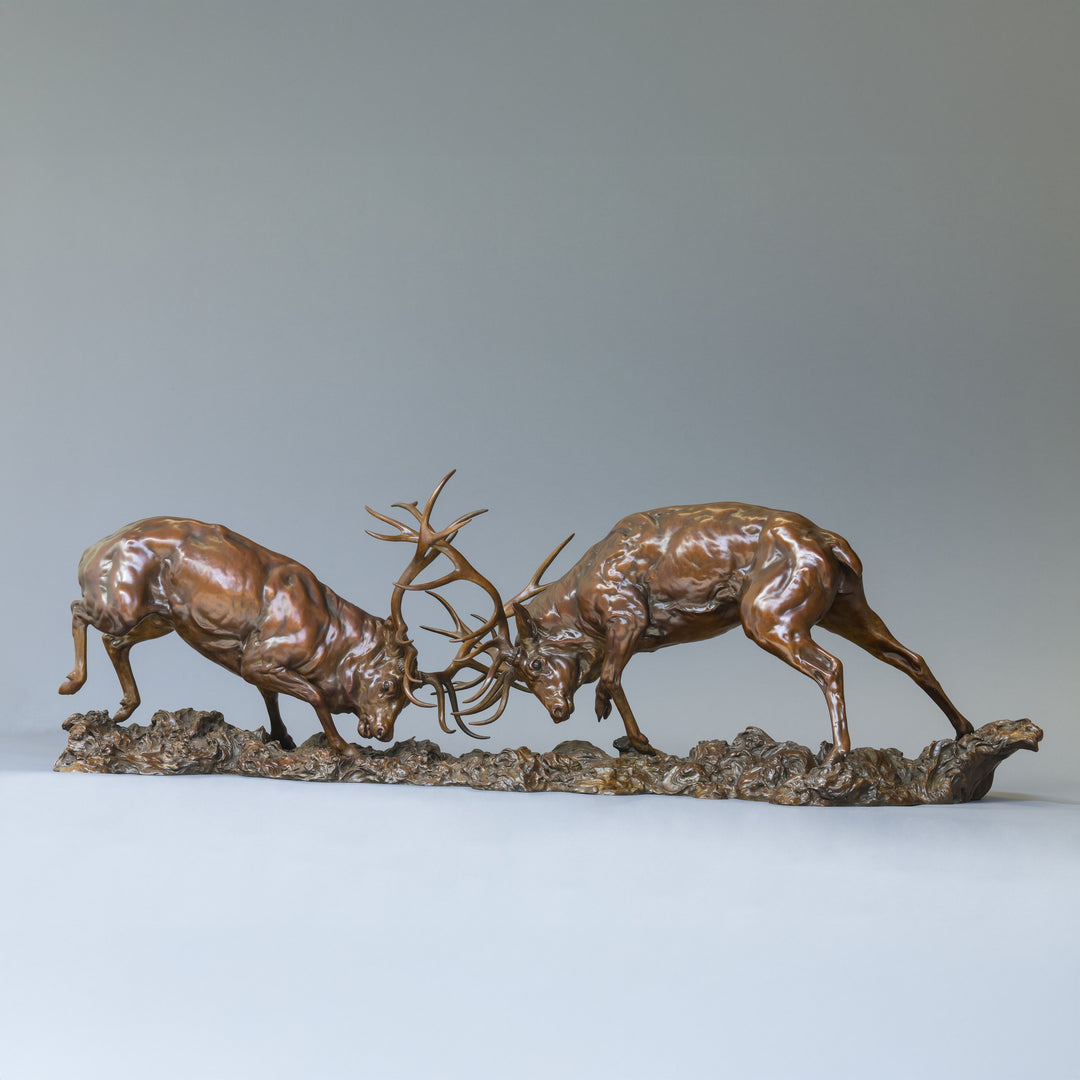 Bronze sculpture of two red deer stags in mid-rut, antlers locked in a dynamic head-to-head clash, highly detailed musculature and patina, mounted on a textured bronze base.