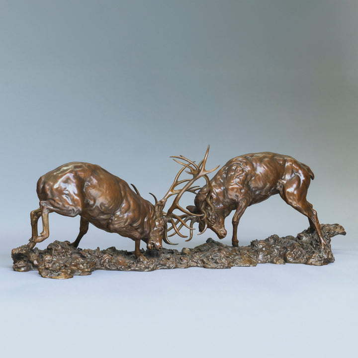 Bronze sculpture of two red deer stags in mid-rut, antlers locked in a dynamic head-to-head clash, highly detailed musculature and patina, mounted on a textured bronze base.
