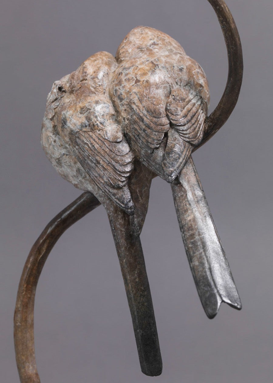 A delicate bronze sculpture of two long-tailed tits nestled together on a sweeping branch, their rounded forms and soft patinated tones capturing warmth, intimacy and the gentle character of these much-loved British birds.
