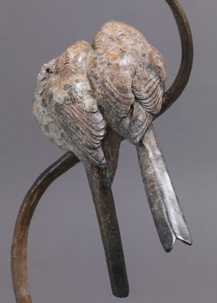A delicate bronze sculpture of two long-tailed tits nestled together on a sweeping branch, their rounded forms and soft patinated tones capturing warmth, intimacy and the gentle character of these much-loved British birds.