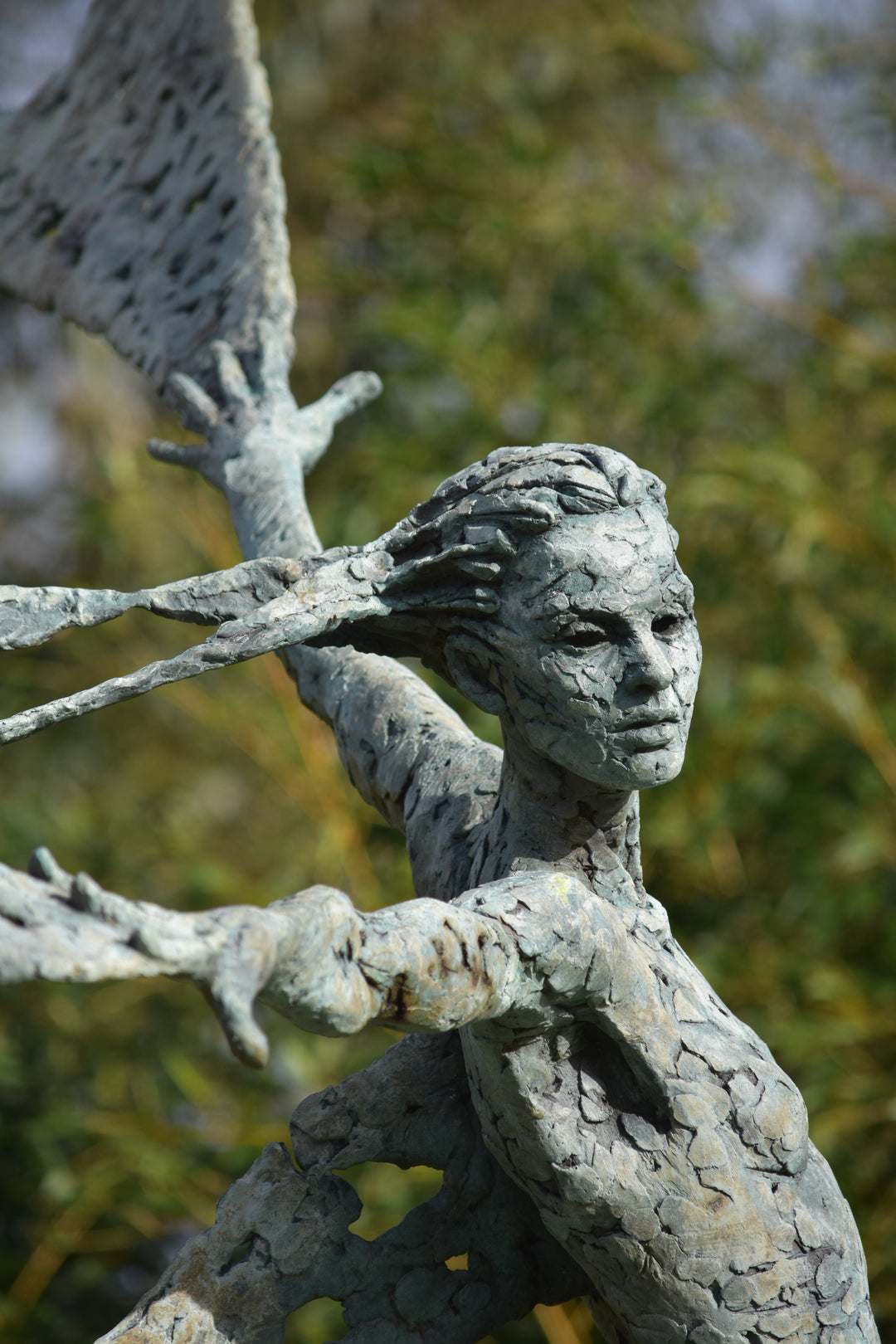 Monumental bronze sculpture of Theia, Greek goddess of light, portrayed in an elegant, elongated form with flowing limbs and wing-like extensions. Her textured surface and dynamic pose evoke movement and radiance, with light-catching shards projecting from her figure against open sky and landscape.