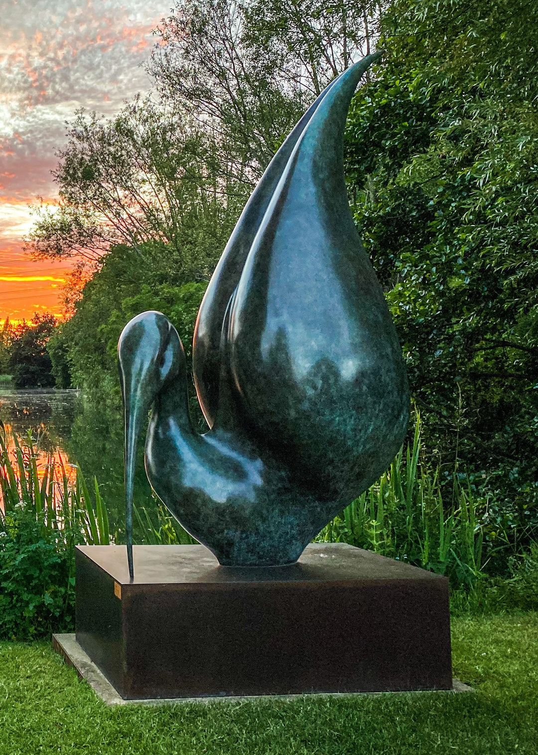 Simon Gudgeon bronze sculpture Thoth featuring a large scale abstract ibis-inspired form with flowing crescent curves displayed within a landscaped outdoor setting beside water.
