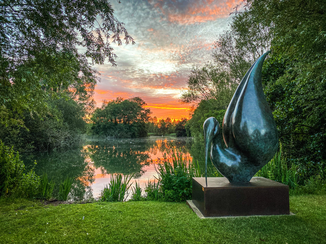Simon Gudgeon bronze sculpture Thoth featuring a large scale abstract ibis-inspired form with flowing crescent curves displayed within a landscaped outdoor setting beside water.