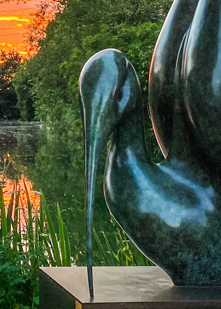 Simon Gudgeon bronze sculpture Thoth featuring a large scale abstract ibis-inspired form with flowing crescent curves displayed within a landscaped outdoor setting beside water.