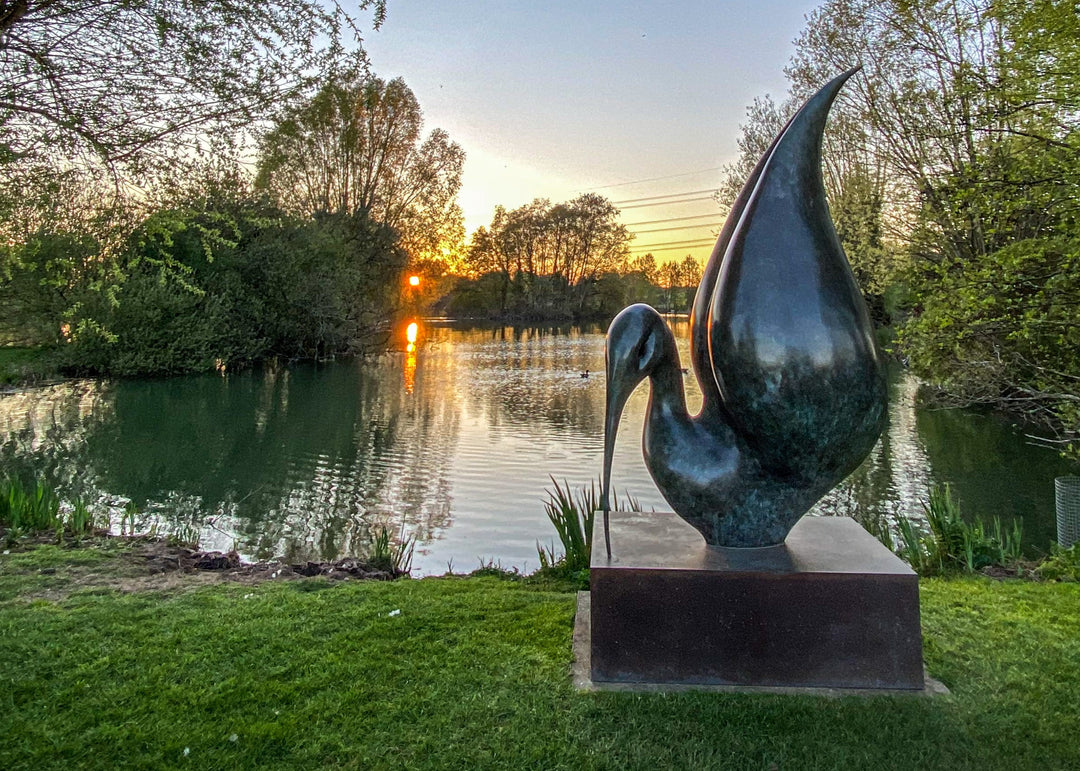 Simon Gudgeon bronze sculpture Thoth featuring a large scale abstract ibis-inspired form with flowing crescent curves displayed within a landscaped outdoor setting beside water.