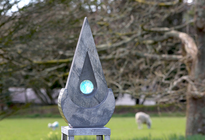 Stacey Beaumont slate and glass sculpture Ti-Pedin, a tall triangular form in reclaimed Delabole and French slate with carved detail and an iridised blue glass centre, inspired by sacred spaces and reflection.
