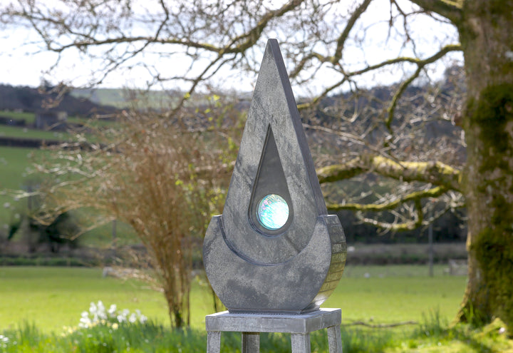 Stacey Beaumont slate and glass sculpture Ti-Pedin, a tall triangular form in reclaimed Delabole and French slate with carved detail and an iridised blue glass centre, inspired by sacred spaces and reflection.