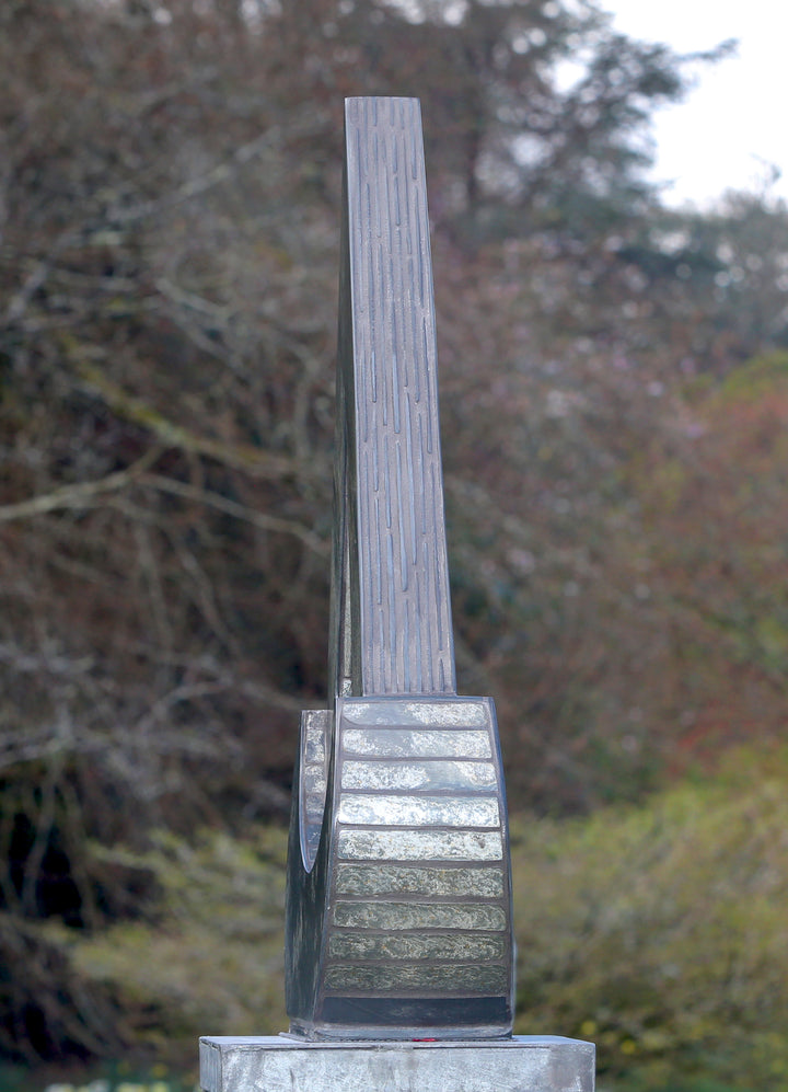 Stacey Beaumont slate and glass sculpture Ti-Pedin, a tall triangular form in reclaimed Delabole and French slate with carved detail and an iridised blue glass centre, inspired by sacred spaces and reflection.