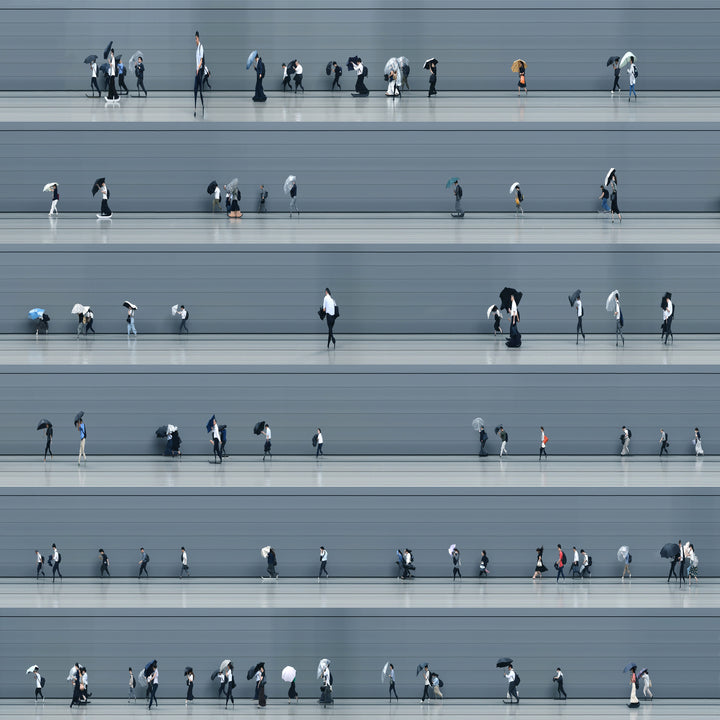A stylised time-slice image of Tokyo commuters struggling against wind and rain during a summer storm. Each figure holds an umbrella as they move across a smooth, steel-grey background—some distorted mid-stride due to the artist’s high-speed video scan technique. The image captures both the uniformity and individuality of city life under pressure.