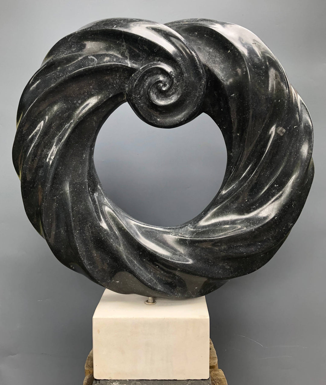 Abstract stone sculpture by Brendan Cullen titled Torque, carved from deep black Kilkenny fossilised limestone with a polished spiral form, mounted on a Purbeck marble base, blending organic movement and meditative balance.