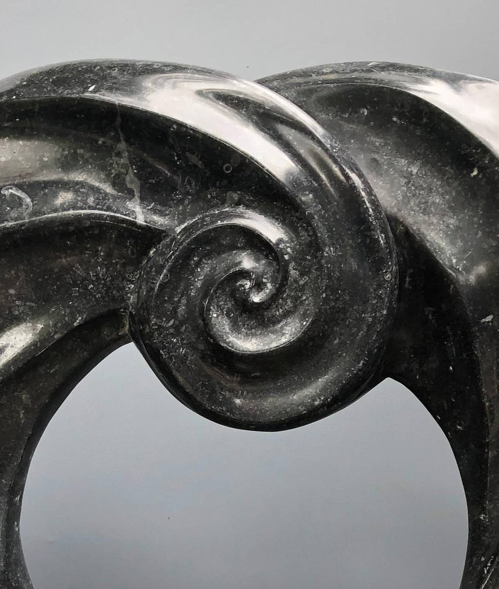 Abstract stone sculpture by Brendan Cullen titled Torque, carved from deep black Kilkenny fossilised limestone with a polished spiral form, mounted on a Purbeck marble base, blending organic movement and meditative balance.