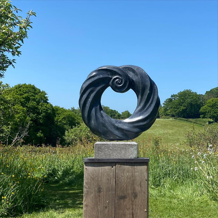 Abstract stone sculpture by Brendan Cullen titled Torque, carved from deep black Kilkenny fossilised limestone with a polished spiral form, mounted on a Purbeck marble base, blending organic movement and meditative balance.