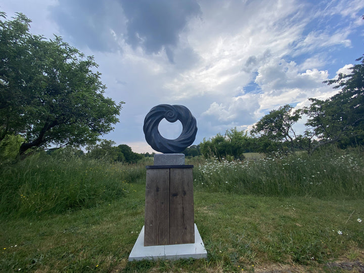 Abstract stone sculpture by Brendan Cullen titled Torque, carved from deep black Kilkenny fossilised limestone with a polished spiral form, mounted on a Purbeck marble base, blending organic movement and meditative balance.