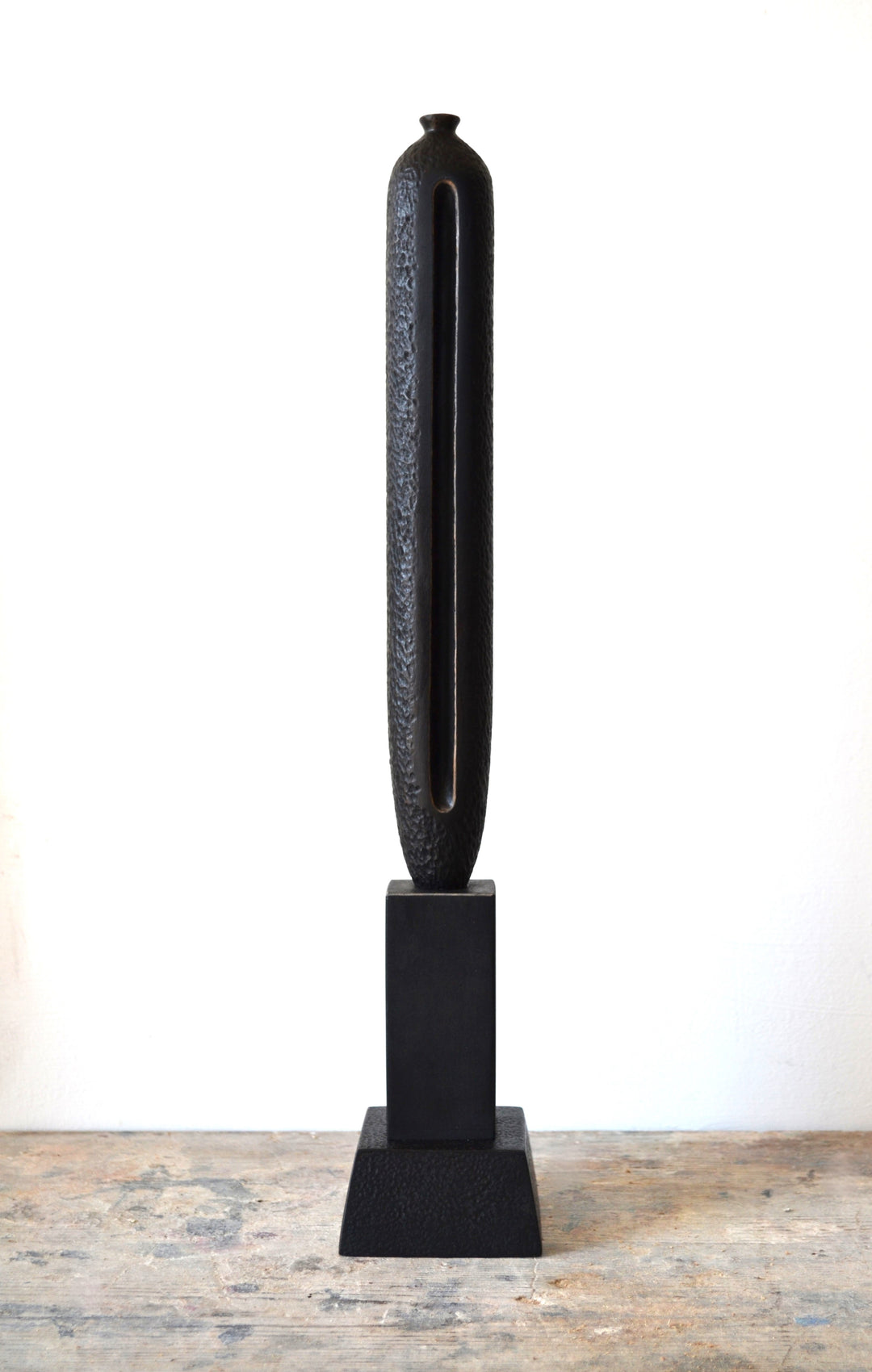 TORR by Nicola Beattie – tall, slender walnut sculpture with textured, rounded form and deep central vertical recess, mounted on a solid stepped base. Rich dark brown finish with natural grain, evoking ancient totems and minimalist modern design.