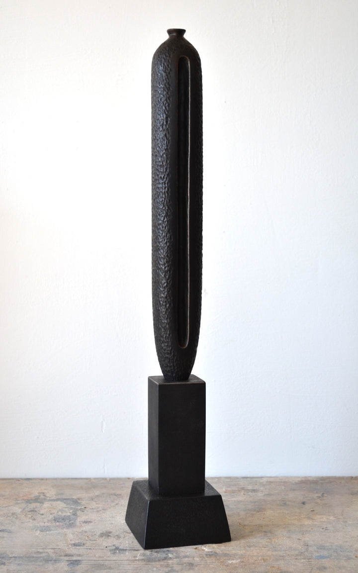 TORR by Nicola Beattie – tall, slender walnut sculpture with textured, rounded form and deep central vertical recess, mounted on a solid stepped base. Rich dark brown finish with natural grain, evoking ancient totems and minimalist modern design.