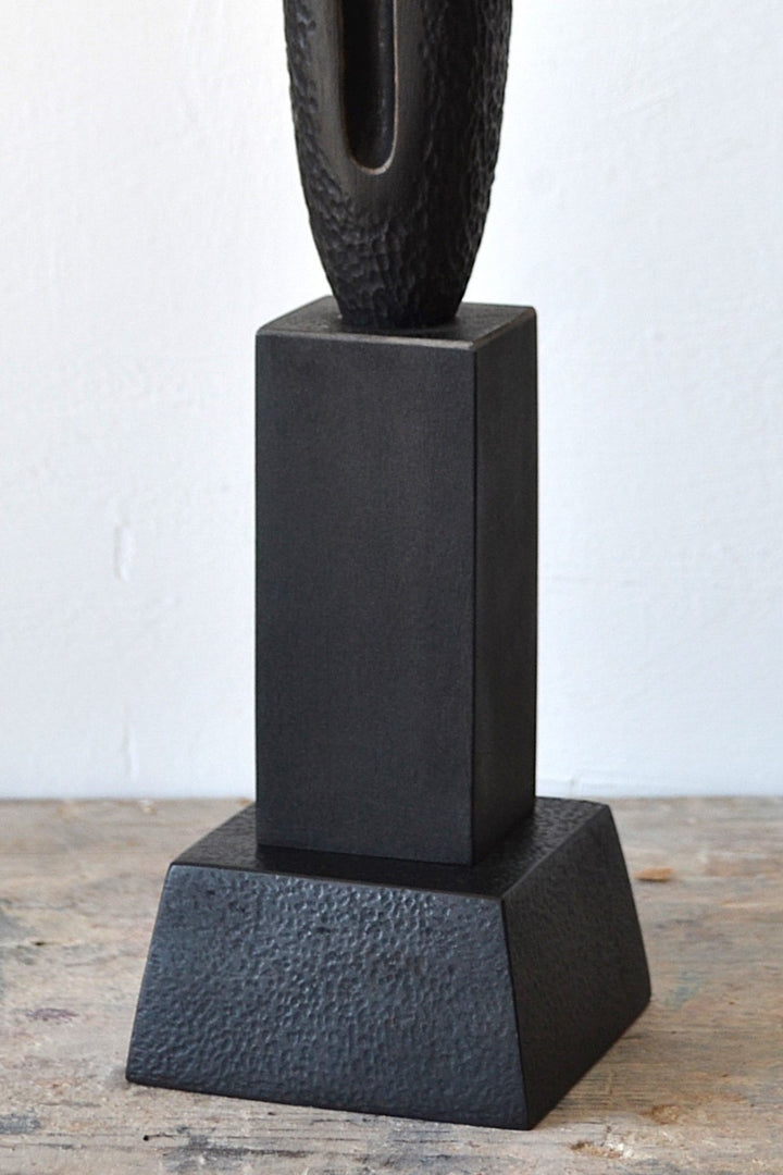 TORR by Nicola Beattie – tall, slender walnut sculpture with textured, rounded form and deep central vertical recess, mounted on a solid stepped base. Rich dark brown finish with natural grain, evoking ancient totems and minimalist modern design.
