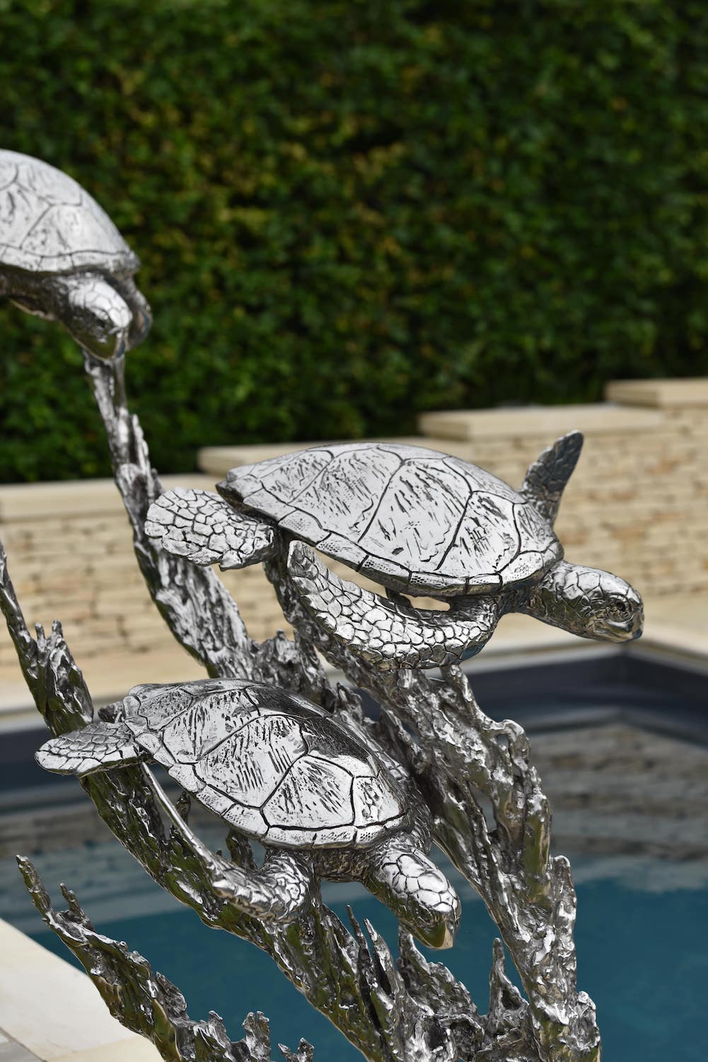 ‘Turtles Stainless Steel’ by Hamish Mackie, a limited-edition marine-grade stainless steel wildlife sculpture depicting three life-size sea turtles swimming through an intricate arrangement of underwater foliage. The polished silver-grey finish highlights the turtles' detailed shells, textured flippers and graceful movement, while the sweeping, branching forms create a sense of flowing water. Mounted on a rectangular stainless steel base, this contemporary sculpture is suitable for indoor or outdoor display