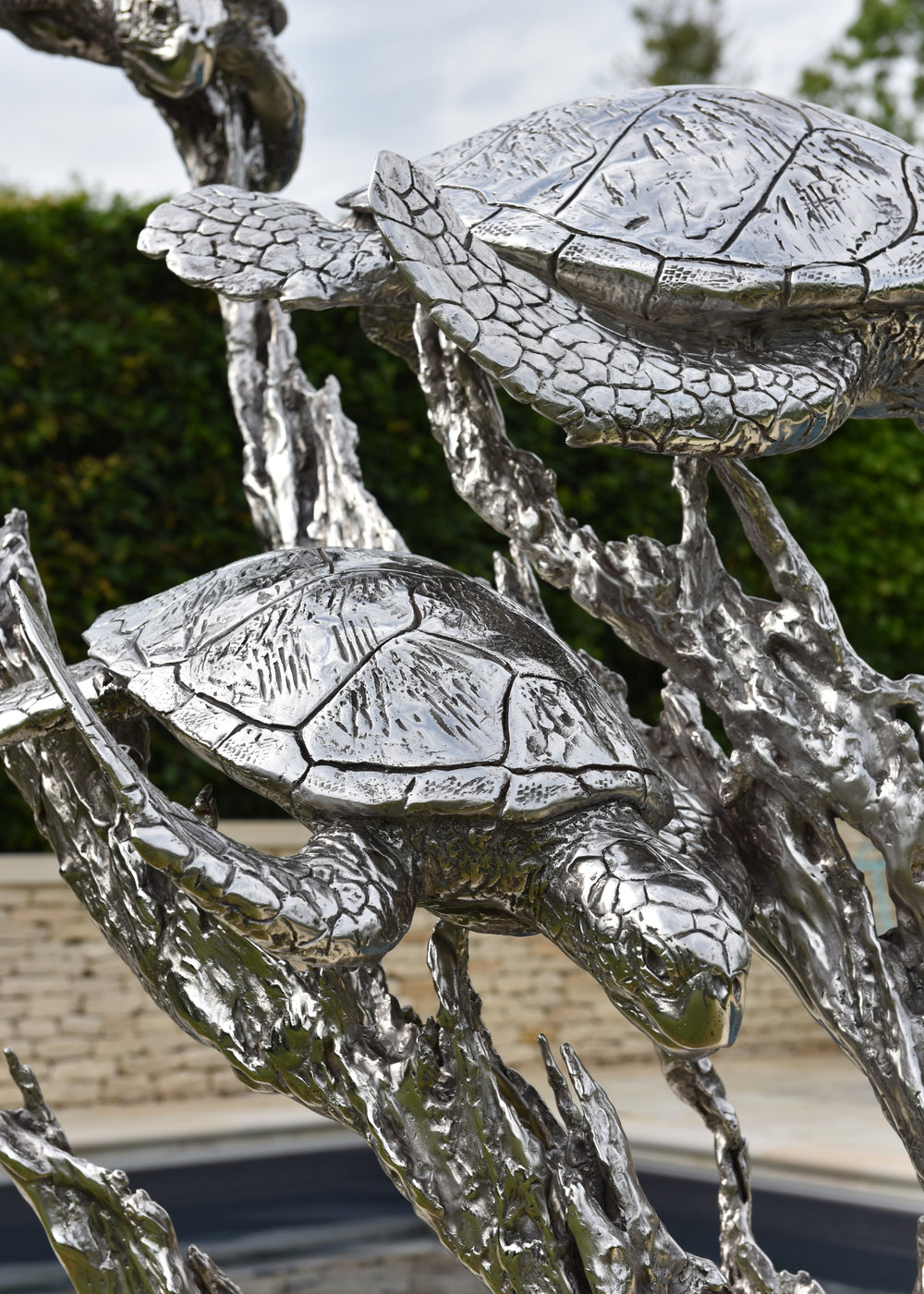 ‘Turtles Stainless Steel’ by Hamish Mackie, a limited-edition marine-grade stainless steel wildlife sculpture depicting three life-size sea turtles swimming through an intricate arrangement of underwater foliage. The polished silver-grey finish highlights the turtles' detailed shells, textured flippers and graceful movement, while the sweeping, branching forms create a sense of flowing water. Mounted on a rectangular stainless steel base, this contemporary sculpture is suitable for indoor or outdoor display