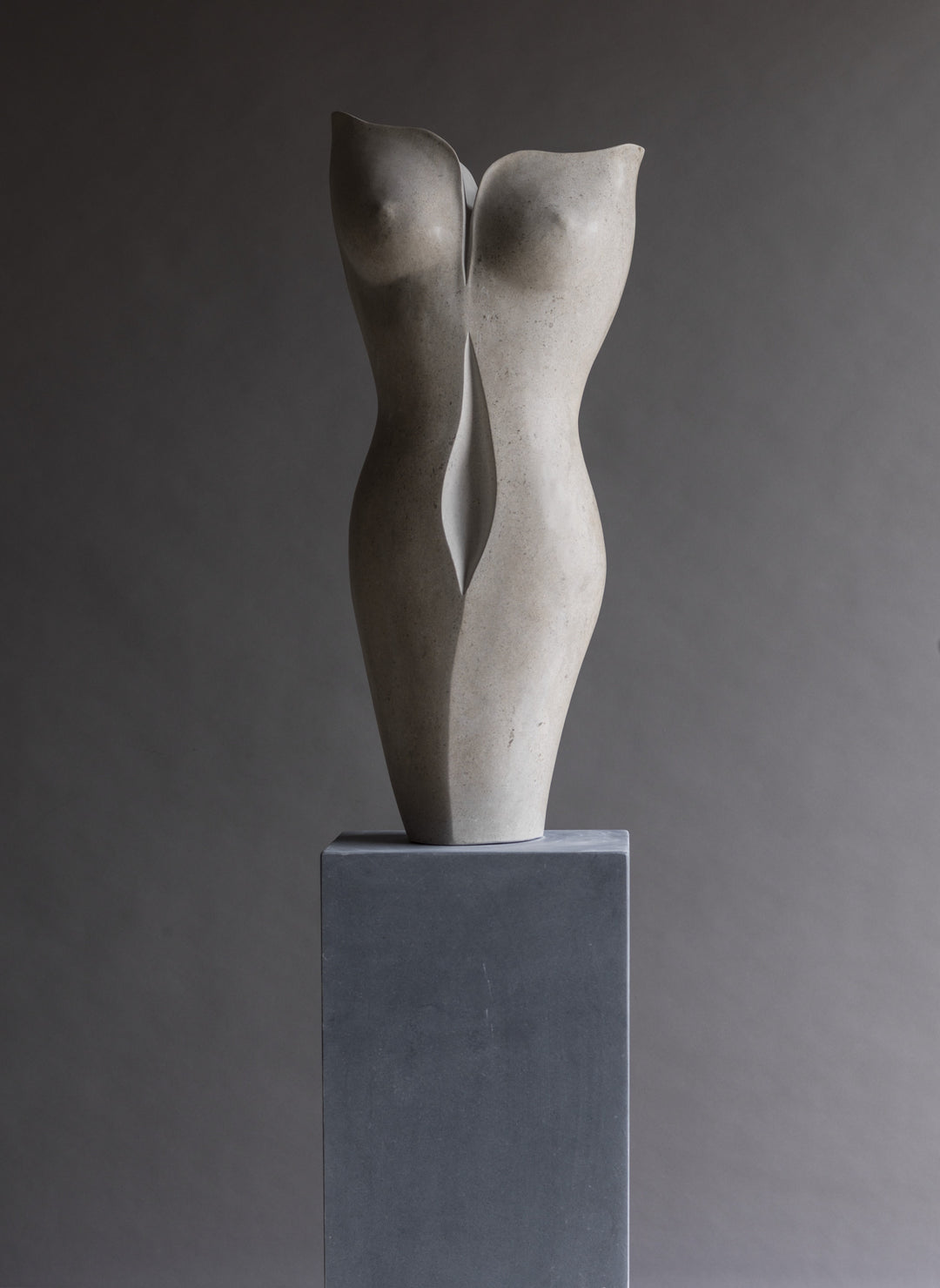“TUTUA” by Lucy Unwin — an elegant hand-carved sculpture in pale Hopton Wood Stone, featuring two seamlessly joined, abstracted female torsos with soft curves and a refined, flowing silhouette, standing on a smooth grey plinth against a neutral backdrop.