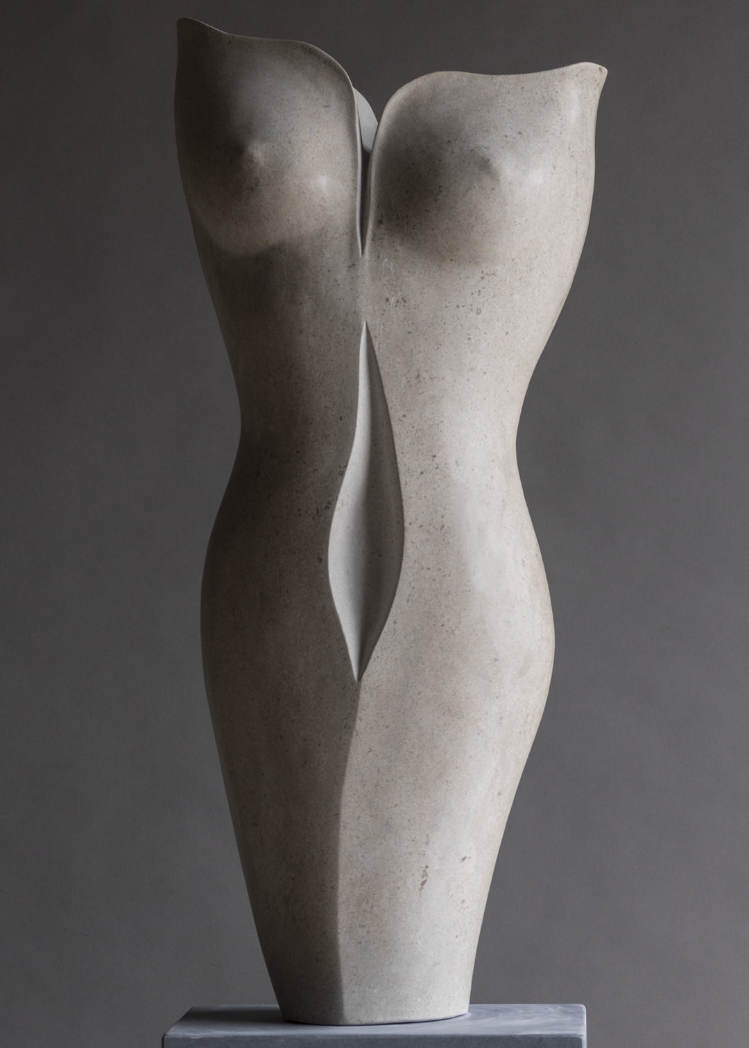 “TUTUA” by Lucy Unwin — an elegant hand-carved sculpture in pale Hopton Wood Stone, featuring two seamlessly joined, abstracted female torsos with soft curves and a refined, flowing silhouette, standing on a smooth grey plinth against a neutral backdrop.