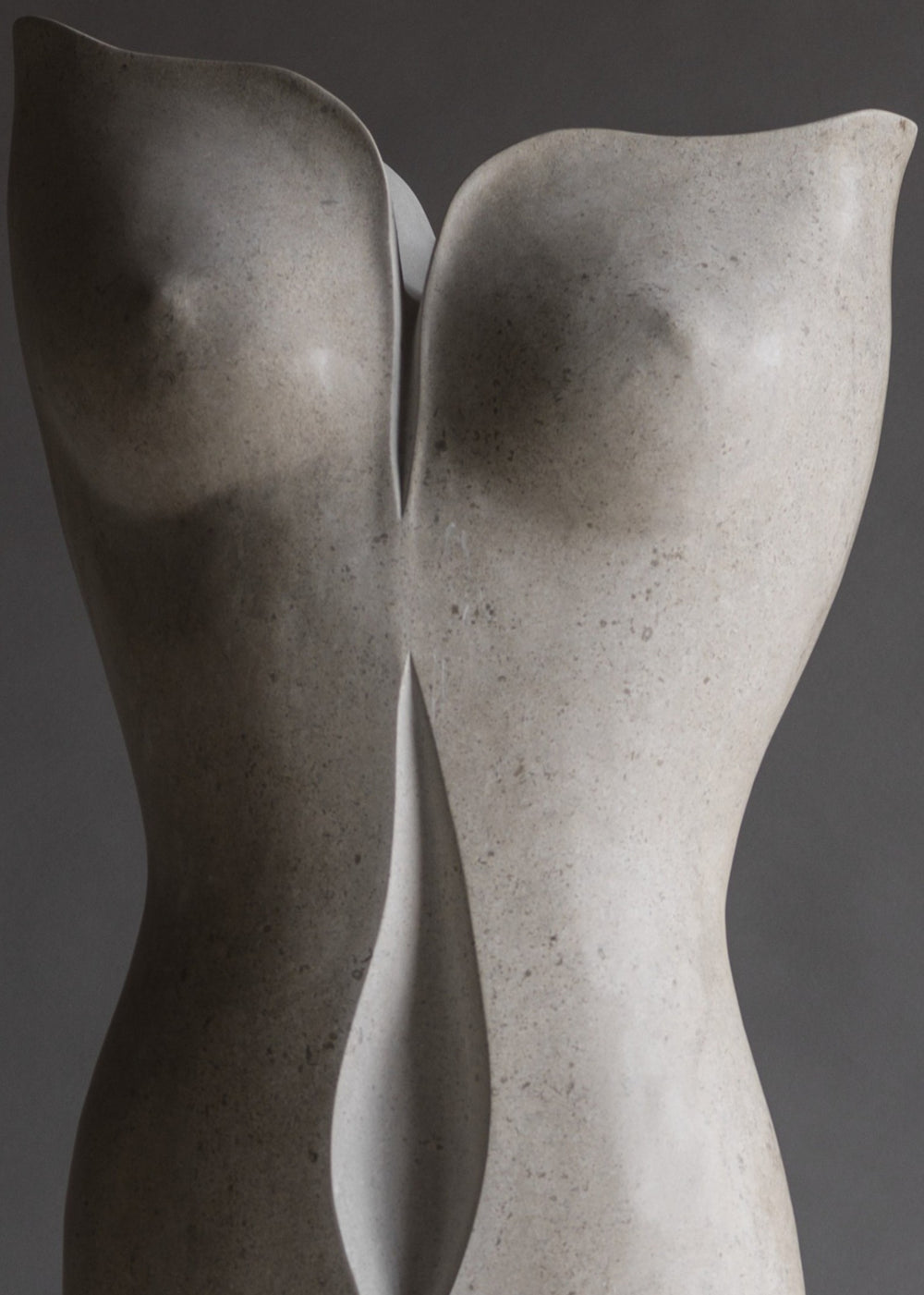 “TUTUA” by Lucy Unwin — an elegant hand-carved sculpture in pale Hopton Wood Stone, featuring two seamlessly joined, abstracted female torsos with soft curves and a refined, flowing silhouette, standing on a smooth grey plinth against a neutral backdrop.