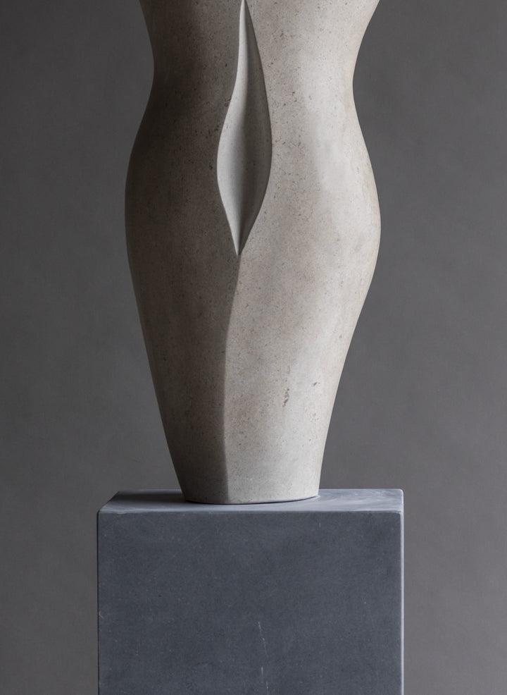 “TUTUA” by Lucy Unwin — an elegant hand-carved sculpture in pale Hopton Wood Stone, featuring two seamlessly joined, abstracted female torsos with soft curves and a refined, flowing silhouette, standing on a smooth grey plinth against a neutral backdrop.