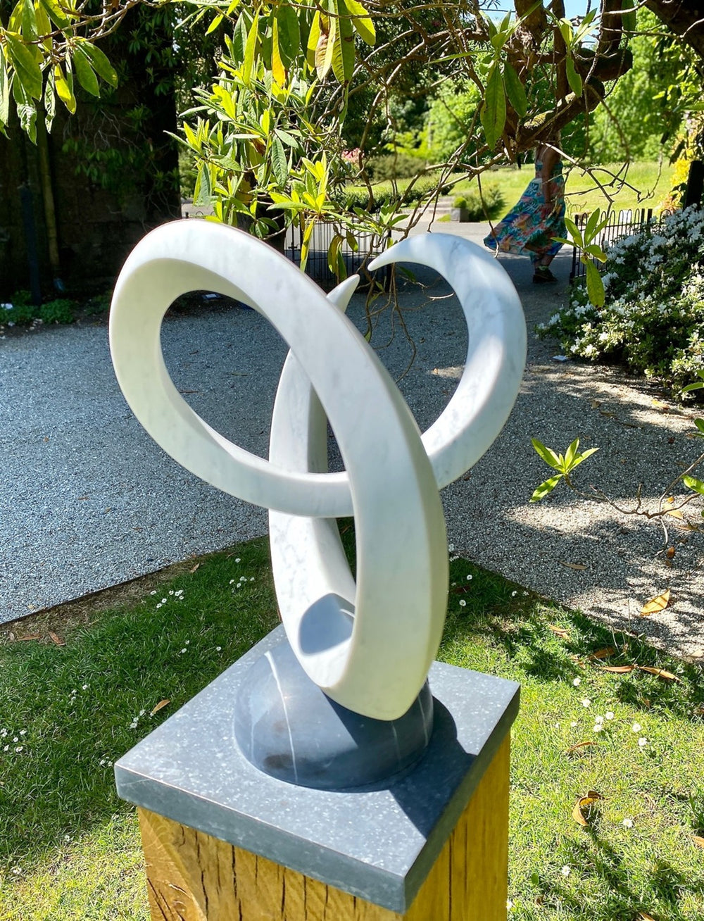 Abstract marble sculpture Twin Peaks – 2025 by Hamish Holman, hand-carved from Carrara marble into two interlocking looping peaks with smooth white veined stone, mounted on a dark stone base for contrast.