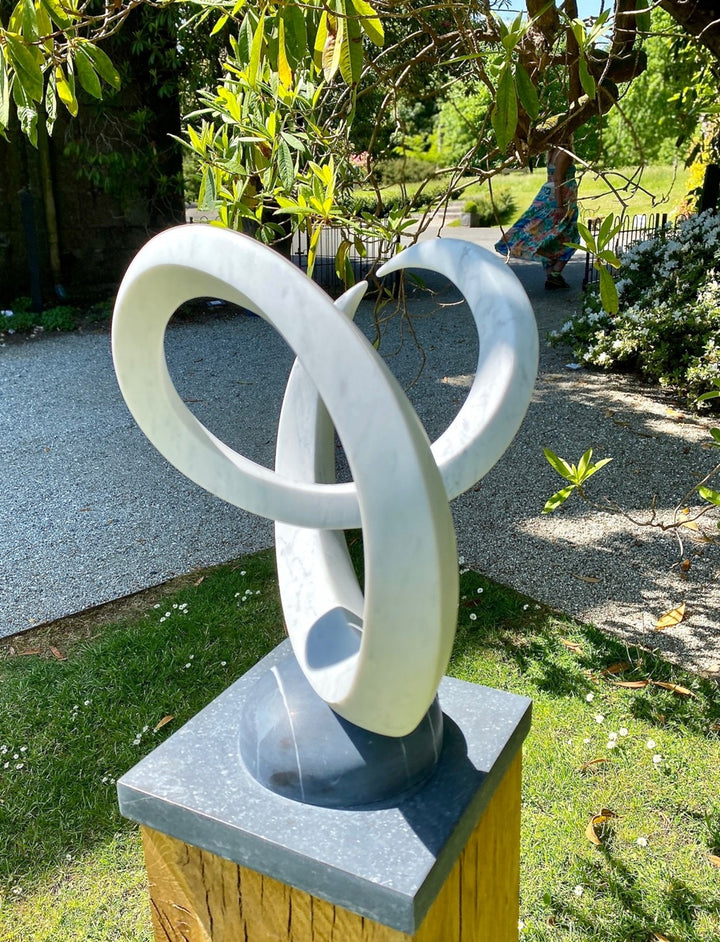 Abstract marble sculpture Twin Peaks – 2025 by Hamish Holman, hand-carved from Carrara marble into two interlocking looping peaks with smooth white veined stone, mounted on a dark stone base for contrast.