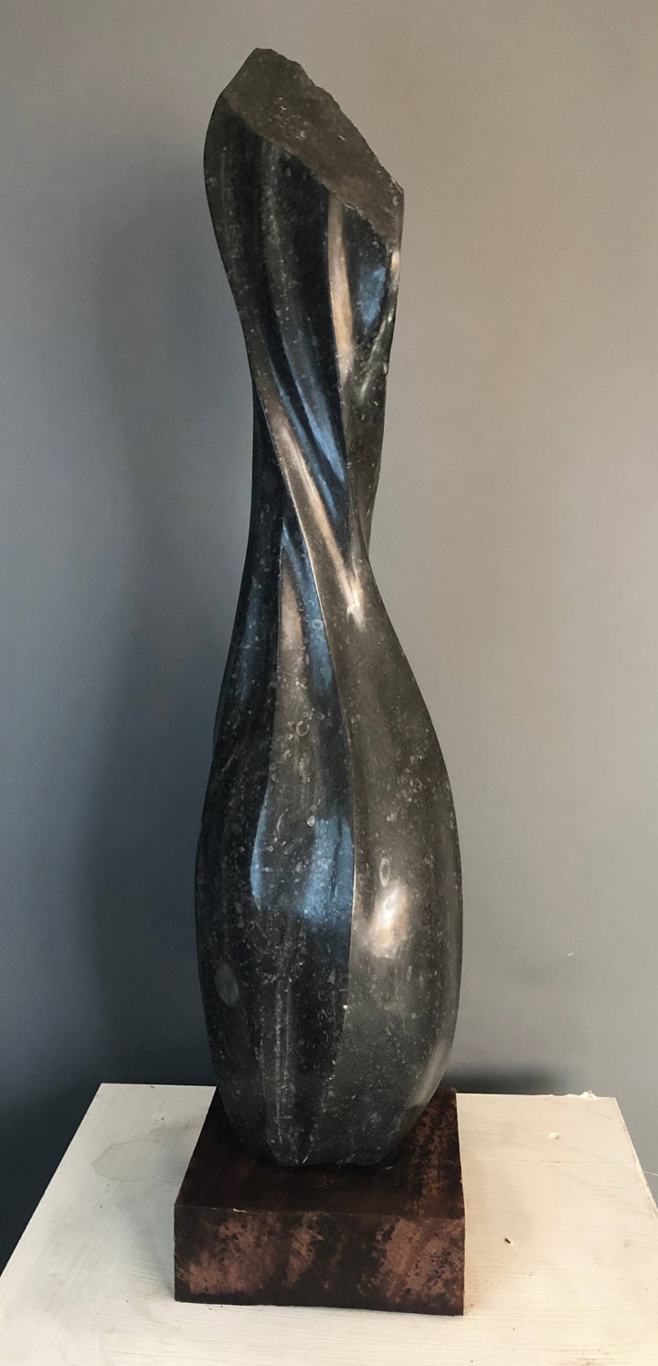 Twist by Brendan Cullen, a hand-carved Kilkenny limestone sculpture featuring a tall, elegant form with smooth, spiralling curves rising from a rounded base, the surface polished to reveal subtle fossil textures within the dark stone.
