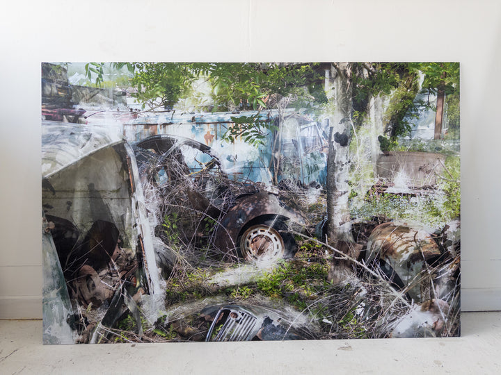 A layered, semi-surreal image of an overgrown car graveyard, where rusted vintage vehicles, tangled branches, and decaying metal parts intertwine with encroaching greenery. A faded turquoise van, oxidised car doors, and fragmented bonnets merge into a dreamlike scene, partially obscured by soft, chemical-like textures and ghostly double exposures.