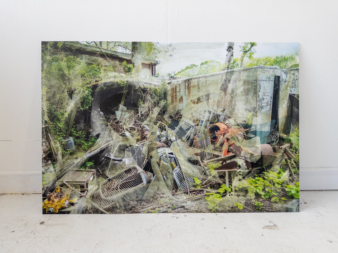 A chaotic yet painterly scene of an abandoned scrapyard, where rusted engine parts, dismantled grilles, and decayed industrial objects lie strewn across the ground. Overgrown vegetation pierces through the debris, while ghost-like layers of metal and machinery are softened by textured overlays and chemical surface treatments. The faded lettering on a derelict lorry hints at its forgotten past, creating a compelling juxtaposition between mechanical ruin and encroaching nature.