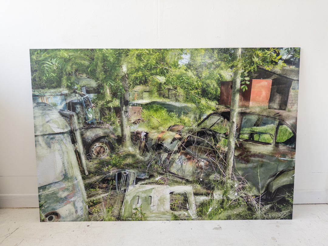An eerie yet poetic composition of rusted cars and disused vehicle parts overtaken by wild greenery. Trees grow through corroded bonnets and windshields, while a faded red structure peeks through the foliage. Soft overlays and chemical-like textures give the scene a painterly, dreamlike quality—blending dereliction with renewal in a haunting meditation on time and decay.