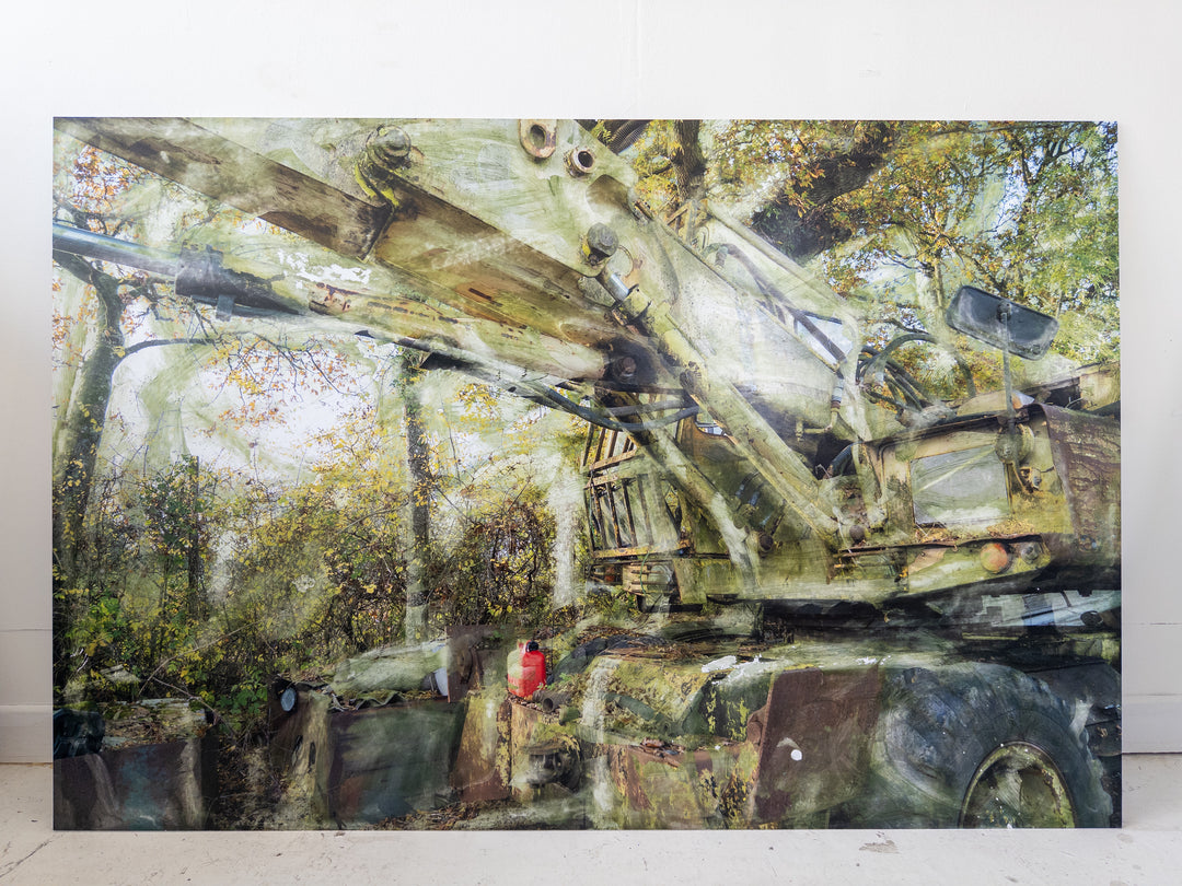 A decaying military-green crane or heavy machinery vehicle sits partially buried in a woodland clearing, its massive hydraulic arms rusted and streaked with oxidised residue. Autumnal foliage surrounds and overlays the scene, while painterly textures and ghosted transparencies give the piece a spectral, timeworn atmosphere. A solitary red fuel container adds a flash of colour against the muted industrial palette.